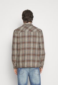 Brun och grå rutigt flanellskjorta med krage, knäppta ärmslut och rak skärning, bärs över blå slitna jeans.