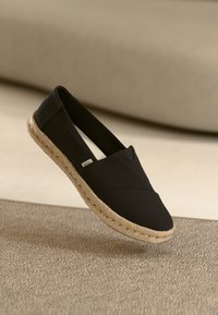 Svart slip-on sko tillverkad av kanvas med en vävd jute-sula. Har en smidig design och låg profil. Texturerad ovandel med minimal söm.