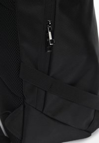 Svart ryggsekk med teksturert stoff, meshpanel og glidelås. Inkluderer justerbare stropper og et slankt design.