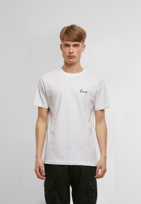 Hvid bomulds T-shirt med korte ærmer, der har et lille sort broderet "skov" logo på venstre bryst. Simpelt, klassisk design.
