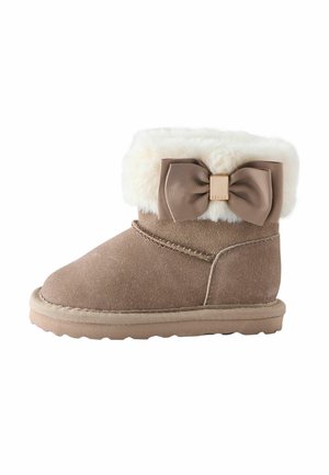 Botte d'hiver pour enfants en daim beige avec bord en fausse fourrure blanche et un nœud décoratif marron sur le côté.