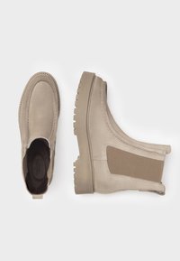 Beige ankelstøvler fremstillet af blødt ruskind, med elastiske sidepaneler og en tekstureret, kraftig sål. Har stikninger langs kanterne.