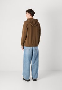 Brun hettegenser med en subtil tekstur og justerbar hette, kombinert med lyseblå vide jeans. Svart fottøy fullfører looken.