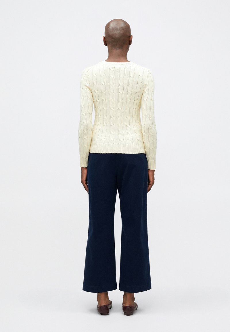 Pull en maille torsadée crème avec un corps ajusté et des manches longues, associé à un pantalon large marine. L'ensemble présente un design simple et épuré.