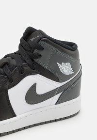 Baskets montantes en cuir noir et blanc, avec un accent gris, une semelle texturée et un logo brodé sur le côté.