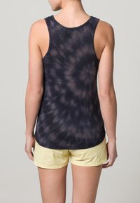 Černý tílko s efektom batikování, kulatým výstřihem a širokými ramínky, vyrobené z lehkého materiálu. V kombinaci se žlutými šortkami, které mají volný střih.
