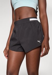 Svarta atletiska shorts i lättviktig tyg, med ett elastiskt midjeband med en vit rand, och en liten vit logotyp på sidan.