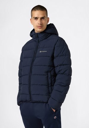 Chaqueta acolchada marina con capucha, que presenta un cierre con cremallera, textura acolchada y un pequeño logo de Champion en el pecho.