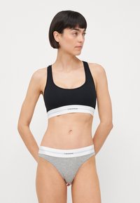 Fekete bordázott sportmelltartó fehér elasztikus pánttal, rajta a "Calvin Klein" logó; szürke pamut tanga, hasonló logós derékpánttal párosítva.