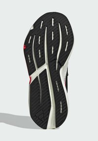 Black athletic shoe sole with textured rubber, white midsole, red accent, and various grooves for traction. Flat and slightly curved design.