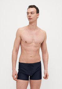 Marineblaue Schwimmshorts aus leichtem Stoff, mit einem Kordelzugbund, einer figurnahen Passform und einer glatten Textur ohne Muster oder Akzente.