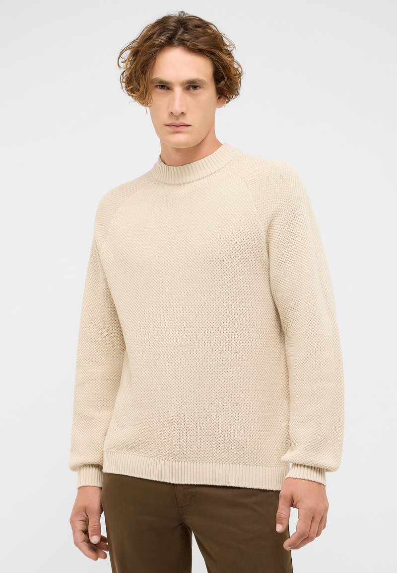 Beige kötött pulóver texturált mintával, kerek nyakkal és bordás mandzsettákkal, valamint alsó szegéllyel. Lazán illeszkedő fazonú, hosszú raglán ujjakkal rendelkezik.