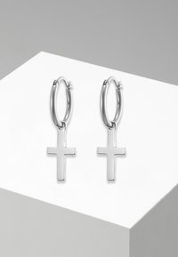 Orecchini a cerchio in argento con una finitura liscia, dotati di un pendente a croce. Il design è circolare con una superficie lucida e riflettente.