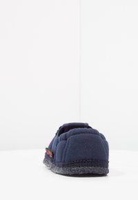 Navyblauwe slipper van textiel, met een ronde achterkant en een grijze rubberen zool. Bevat een rood logolabel aan de zijkant voor extra detail.