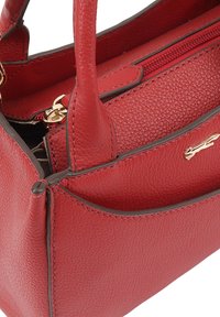 Rode leren handtas met een textuur, voorzien van twee korte handvatten, een ritsvak en een goudkleurig logo accent.