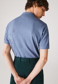 Ljusblå kortärmad polo skjorta, tillverkad av stickat tyg. Bärs med höga mörkgröna byxor som har bakfickor och bälteshällor.