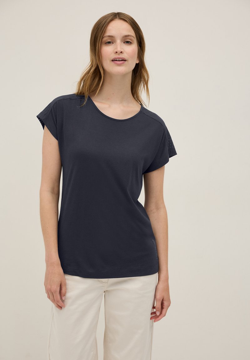 Chemise à manches courtes bleu marine foncé avec un col rond, texture lisse et détails de couture subtils, associée à un pantalon large de couleur claire.