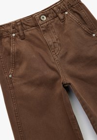 Bruine ribfluweel broek met een gestructureerde afwerking, voorzien van vijf zakken, riemlussen en metalen hardware voor sluiting en accenten.