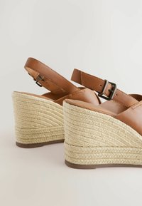 Brown leather wedge sandals with a woven jute heel. Adjustable ankle strap and textured surface. Features a contoured shape and durable sole.