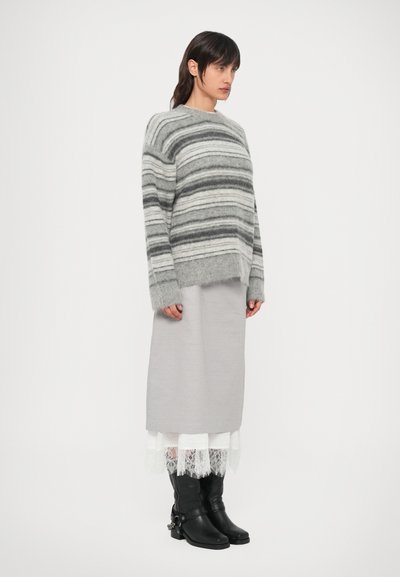 Triibuline hall kampsun, millel on laiad varrukad, kantud üle pika helehalli seeliku. Mustad põlveni ulatuvad saapad pitsdetailiga seeliku ääres.