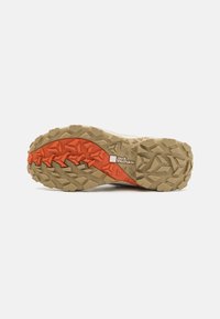 Trail-sko sula med en robust, strukturerad gummiyttersula i beige med orange detaljer och multidirektionella mönster för bättre grepp.