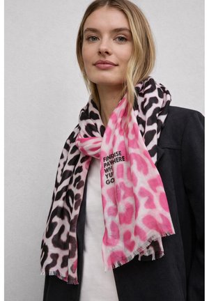 Femme portant un manteau noir et une écharpe à imprimé léopard rose et noir avec le texte "FIND RISE PART HERE WHERE YOU GO" sur un fond uni.