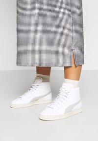 Vita höga sneakers med ett texturerat läderöverdrag och grå detaljer. Har en spräcklig gummisula och snörning. Kjolen har ett hundtandsmönster.