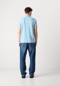 Gaiši zils T-krekls ar īsām piedurknēm, savienots ar vaļīgiem tumši ziliem džinsiem. Krekla piedurknēs ir klasiskā apkakle un smalka tekstūra.