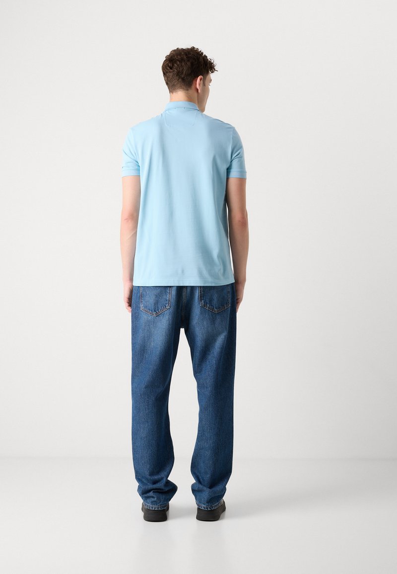 Lichtblauw polo-shirt met korte mouwen, gecombineerd met losse donkerblauwe spijkerbroek. Het shirt heeft een klassieke kraag en een subtiele textuur.