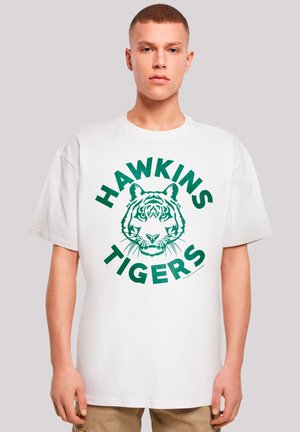 White cotton t-shirt featuring a green graphic of a tiger's face with "HAWKINS TIGERS" text surrounding it in bold letters.
