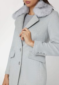 Cappotto in misto lana grigio con collo in pelliccia sintetica, due tasche anteriori, chiusura con un solo bottone e tre bottoni decorativi sui polsini.