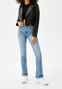 Zwarte cropped leren motorjack met zilverkleurige hardware, gecombineerd met lichtblauwe flare jeans en witte sneakers.
