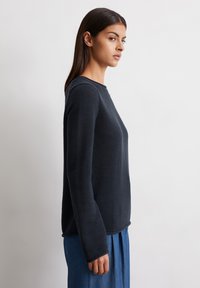 Dunkelblauer, strukturierten Pullover mit Rundhalsausschnitt und langen Ärmeln, kombiniert mit einem blauen Rock. Der Stoff wirkt gerippt und robust.