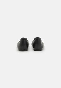 Zapatos de cuero negro con punta redondeada y tacón bajo, que presentan detalles de costura sutiles y un acabado suave.