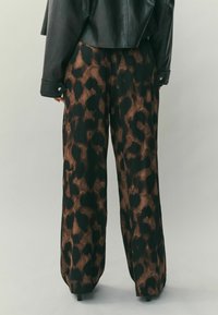 Széles szárú nadrág tigrismintás mintázattal, sötétbarna és fekete színvilággal. Simább textúrájú, rugalmas derékpánttal.