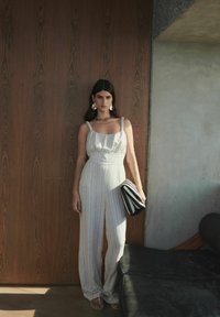 Ljust randig jumpsuit med tunna axelremmar och midja som är åtdragen, i kombination med en svart- och vitrandig clutch och stora örhängen.