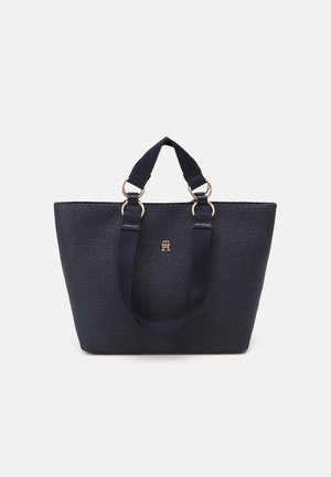 Sac fourre-tout noir texturé avec deux poignées courtes et anneaux dorés, avec un petit logo doré au centre sur fond blanc.