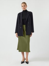 Zwarte double-breasted blazer over een zwarte coltrui, gecombineerd met een olijfgroene satijnen rok tot de knie en zwarte puntige hakken.