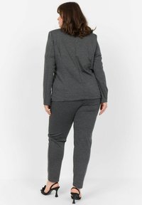 Grå stickad dräkt med en skräddarsydd kavaj och matchande slim-fit byxor. Har långa ärmar och en subtil textur. Svarta högklackade sandaler.