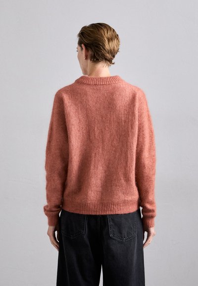 Pink wool sweater with a ribbed neckline and hem. Features a relaxed fit and textured surface. Paired with high-waisted black trousers.