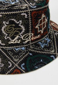 Sort bucket hat med detaljeret flerfarvet broderi, som har mønstre i blå, grøn, orange og hvid med hvide stikninger som accenter.