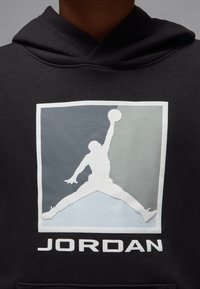 Black hoodie featuring a white Jumpman logo and “JORDAN” text below. Graphic shows an athletic figure in a jumping pose within a colored square.