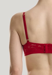 Bralette in pizzo rosso con motivo floreale, spalline regolabili e chiusura a gancio. Finitura in tessuto liscio con bordi ondulati.