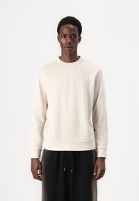 Lys beige sweatshirt med rund hals og lange ermer, med subtilt brodert tekst på forsiden og ribbede mansjetter nederst.