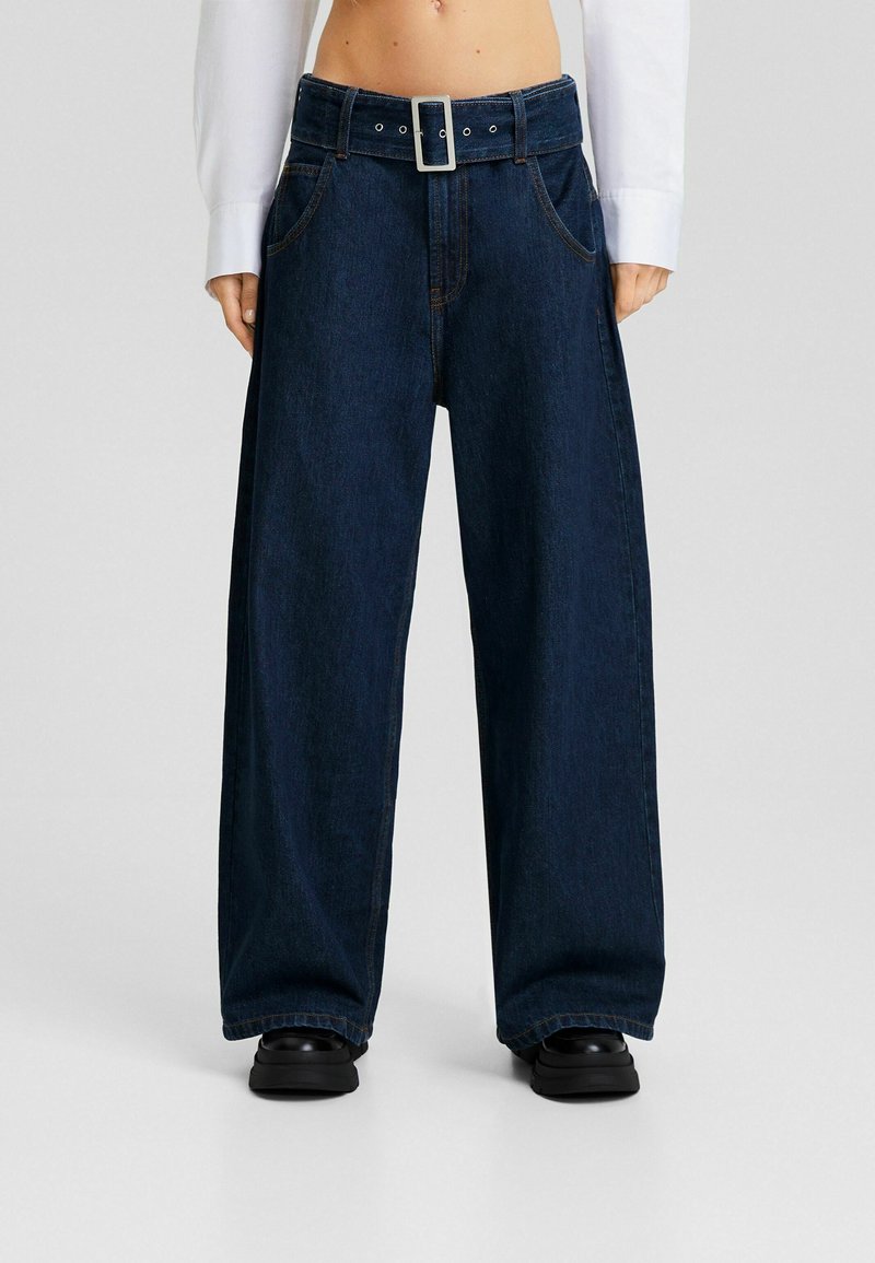 Vidvuxna mörka denimjeans med hög midja och ett stort bälte med silverfärgad spänne. Har framfickor och kontrastsömmar.