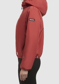 Red padded jacket with a hood, featuring elastic cuffs, a brand logo patch on the sleeve, and a zippered front. Smooth texture, sporty design.