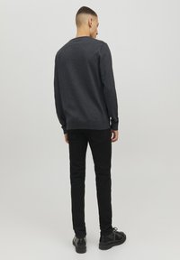 Suéter gris oscuro de manga larga, con puños y dobladillo acanalados, combinado con unos jeans negros ajustados y zapatos negros con cordones, visto desde la parte de atrás.