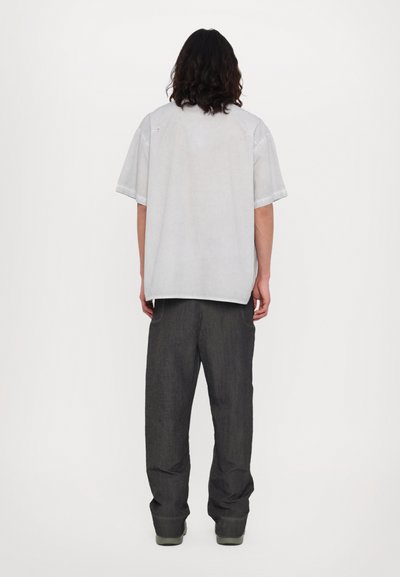 Chemise à manches courtes gris clair avec une coupe décontractée, associée à un pantalon large gris foncé et des chaussures chunky grises. Présente un design simple et minimal.