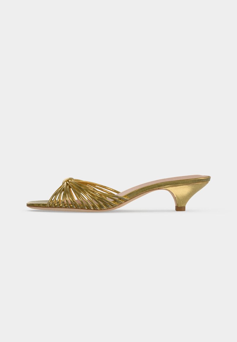 Gold strappy open-toe mule shoe with low kitten heel and knotted design on a plain white background.
