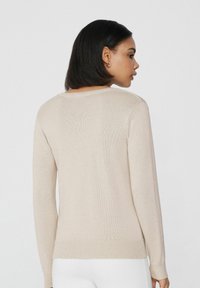 Beige gestrickter Pullover mit langen Ärmeln, Rundhalsausschnitt und elastischem Saum. Die Textur ist glatt und das Material hat ein mittleres Gewicht.